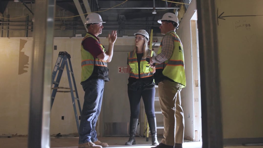 Three construction professionals in safety gear having an on-site discussion, representing women in construction