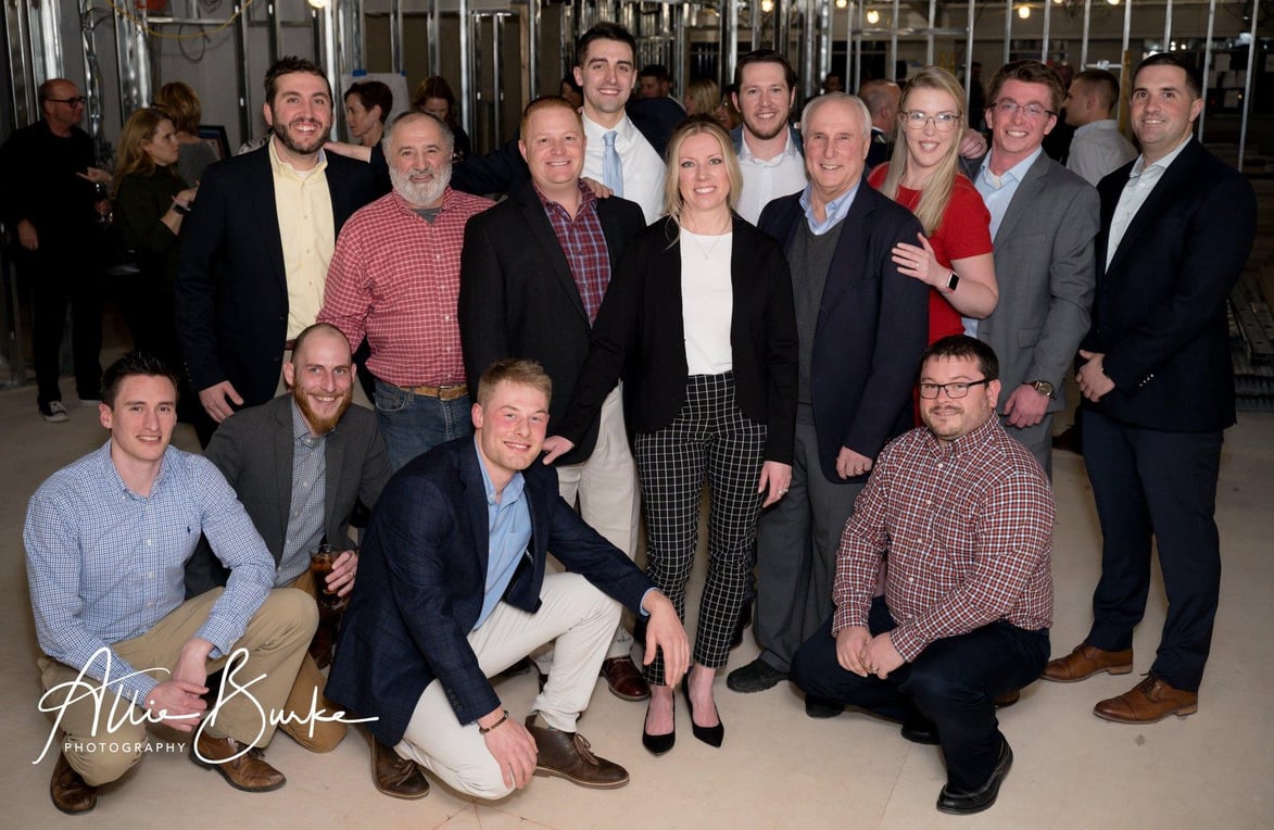 Group photo of the Jewett Construction team and guests posing during a renovation preview event, smiling in a partially finished commercial space.