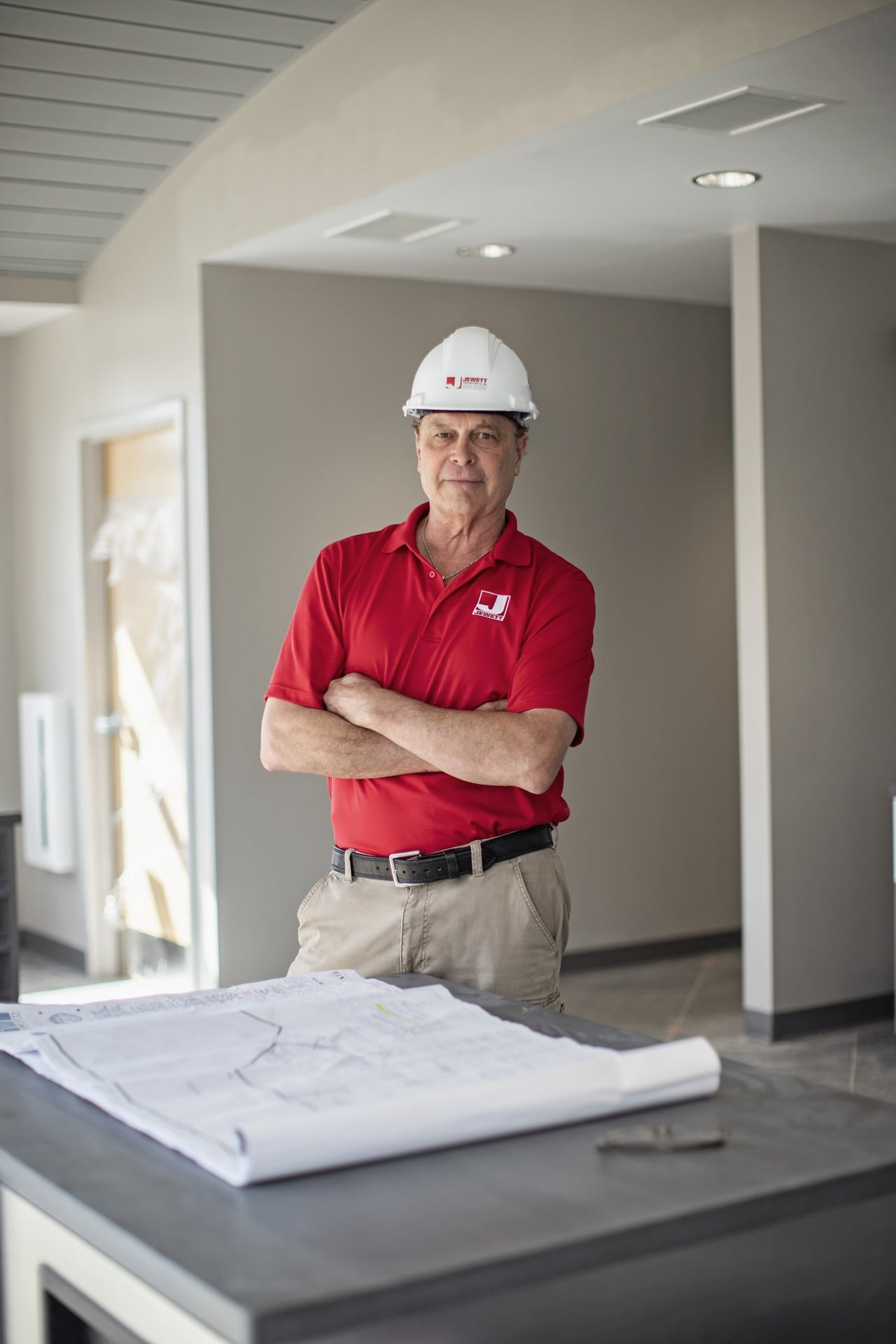Superintendent in Jewett Construction uniform and hard hat standing confidently with project blueprints