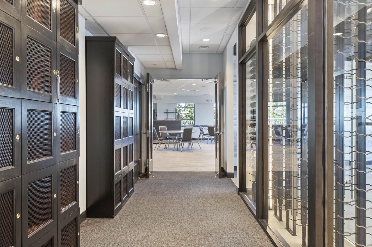 Hallway view of The One Hundred Club featuring custom black lockers, modern wine display, and open lounge area with natural light.