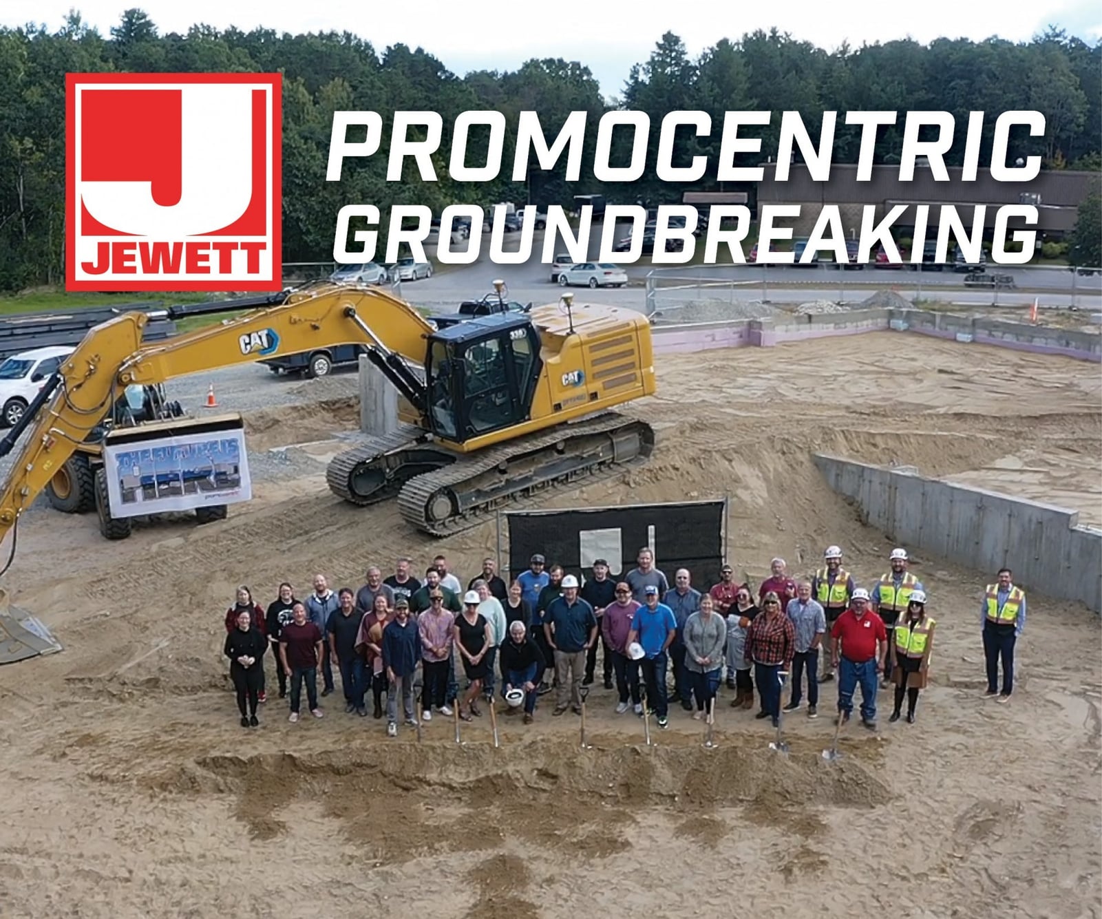 Large group of construction team members and stakeholders pose in front of an excavator at a dirt construction site during the groundbreaking for PromoCentric. Jewett Construction logo appears at the top.