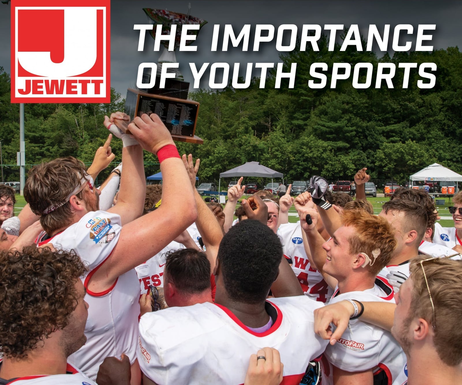 High school football players in white and red uniforms celebrate together on a field, raising a trophy in victory. Surrounded by tents and trees, the team displays excitement and unity. The Jewett Construction logo appears in the top left corner.