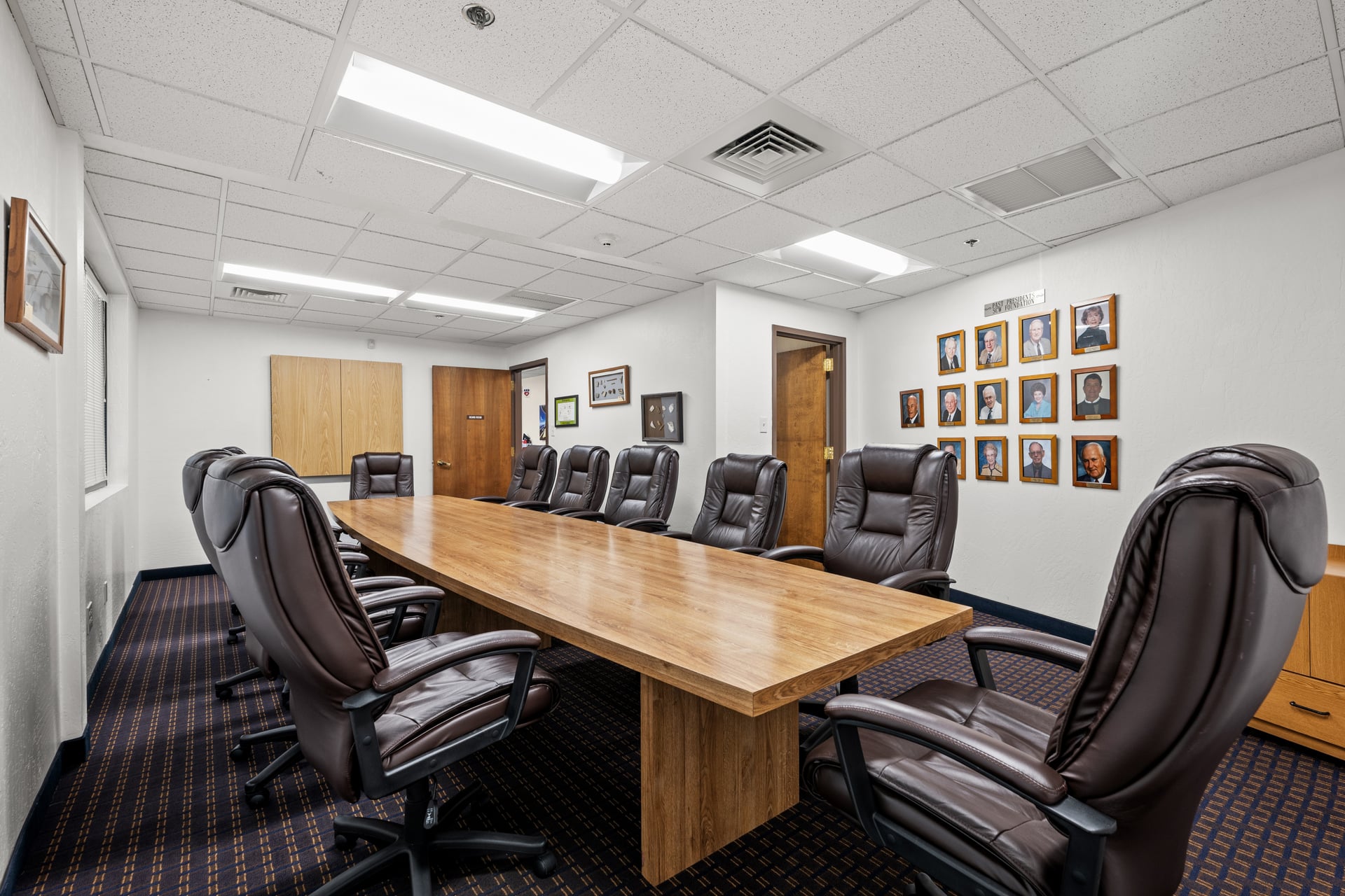 Long rectangular boardroom with 12 leather chairs, wood conference table, and framed portraits on the wall at Sun City West Foundation.