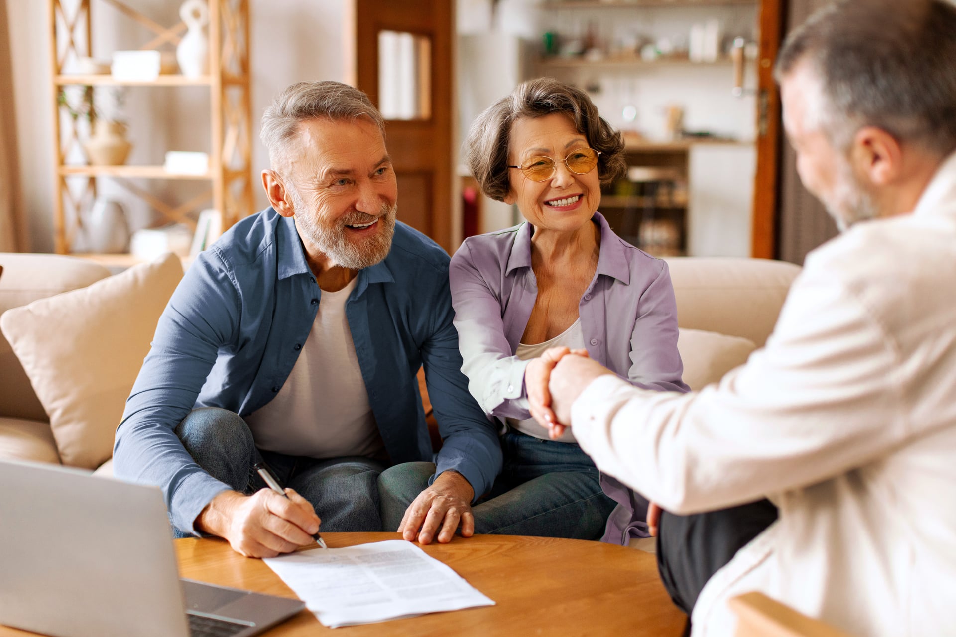 Smiling older couple meeting with a financial advisor at home, reviewing paperwork and shaking hands, symbolizing thoughtful charitable giving and retirement planning.