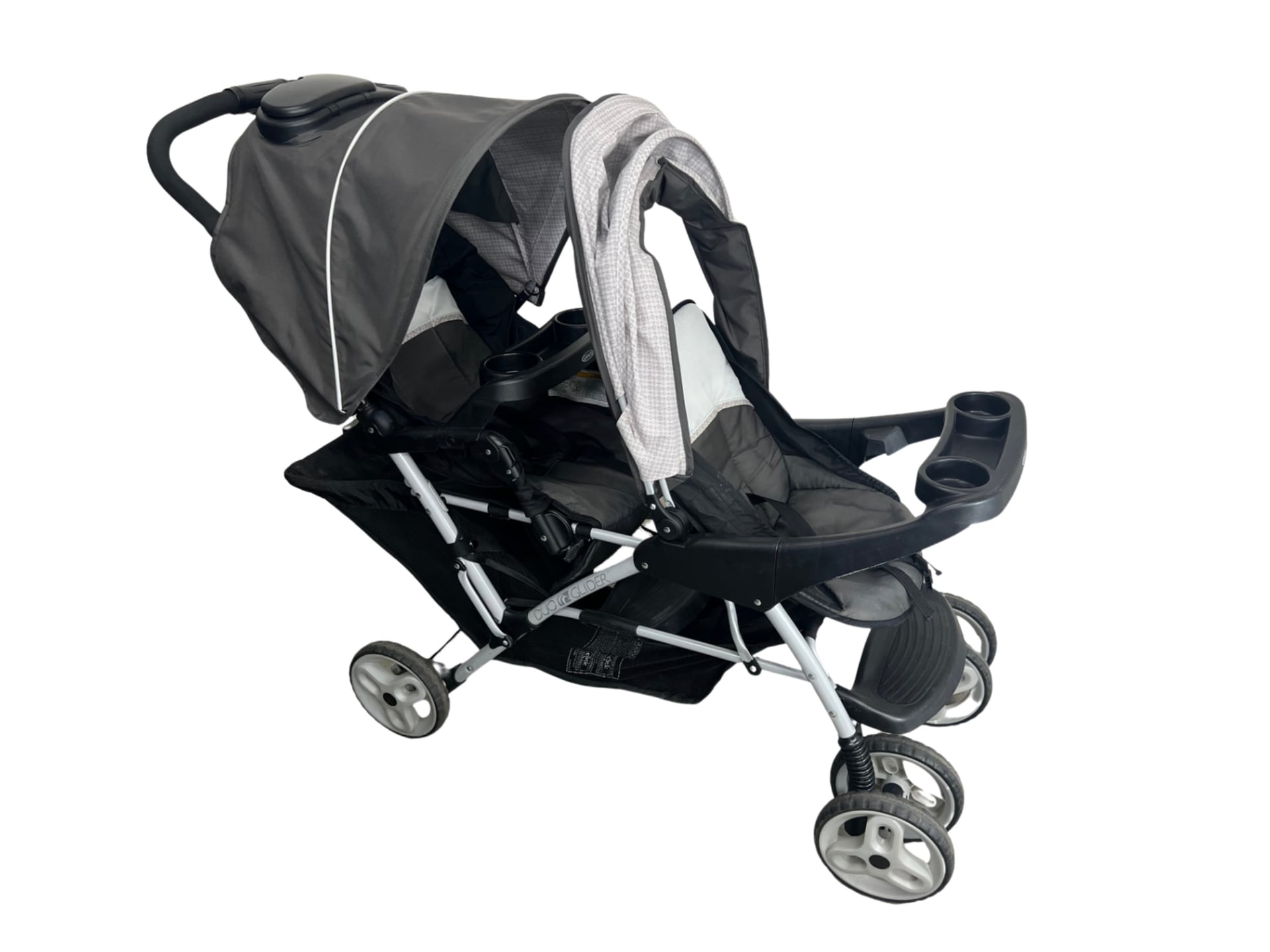 A double stroller with two molded plastic seats, individual adjustable canopies, large rear wheels, and a linkage to fold both seats simultaneously.