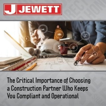 Two professionals reviewing construction documents at a desk with compliance and financial icons overlaid, representing the importance of choosing a construction partner that ensures operational continuity and regulatory compliance. Jewett Construction branding at the top.
