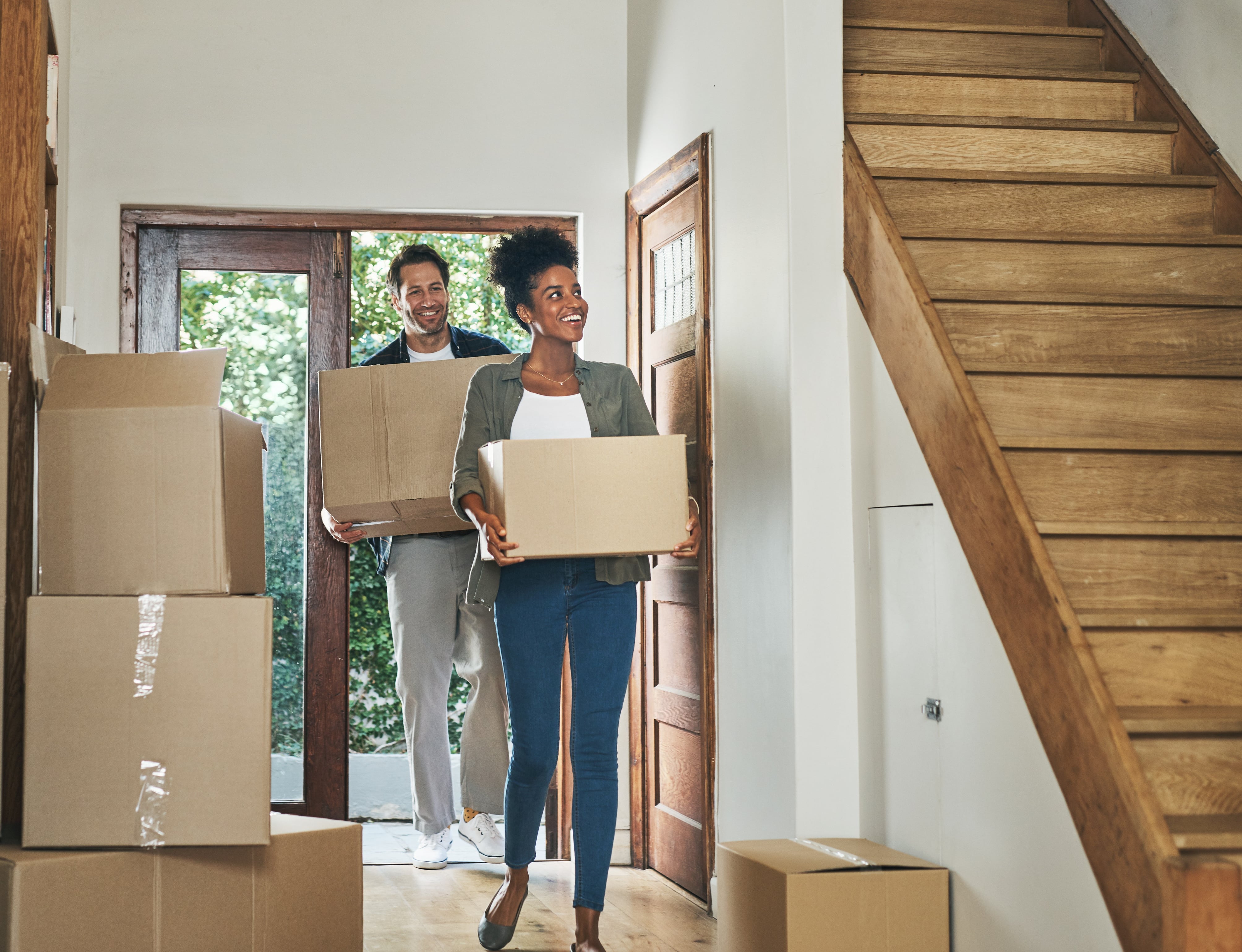Happy couple carrying moving boxes into a new home, symbolizing a successful real estate purchase and fresh start.